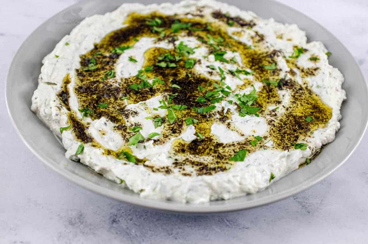 A plate of Haydari yoghurt dip, drizzled with olive oil and dried mint with a large copper spoon sit on a marble tabletop
