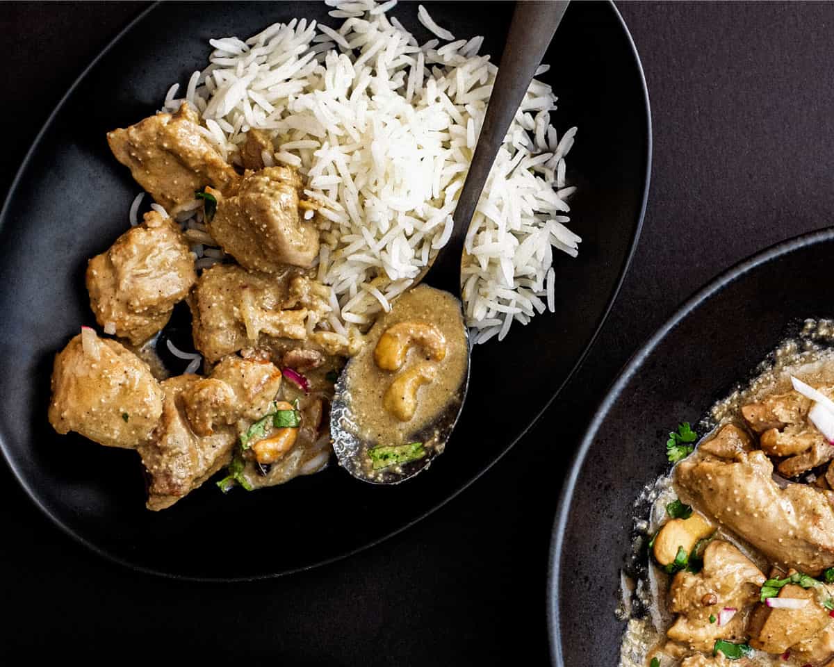 Bengali Rezala Chicken in a black bowl with spoon on a black background.