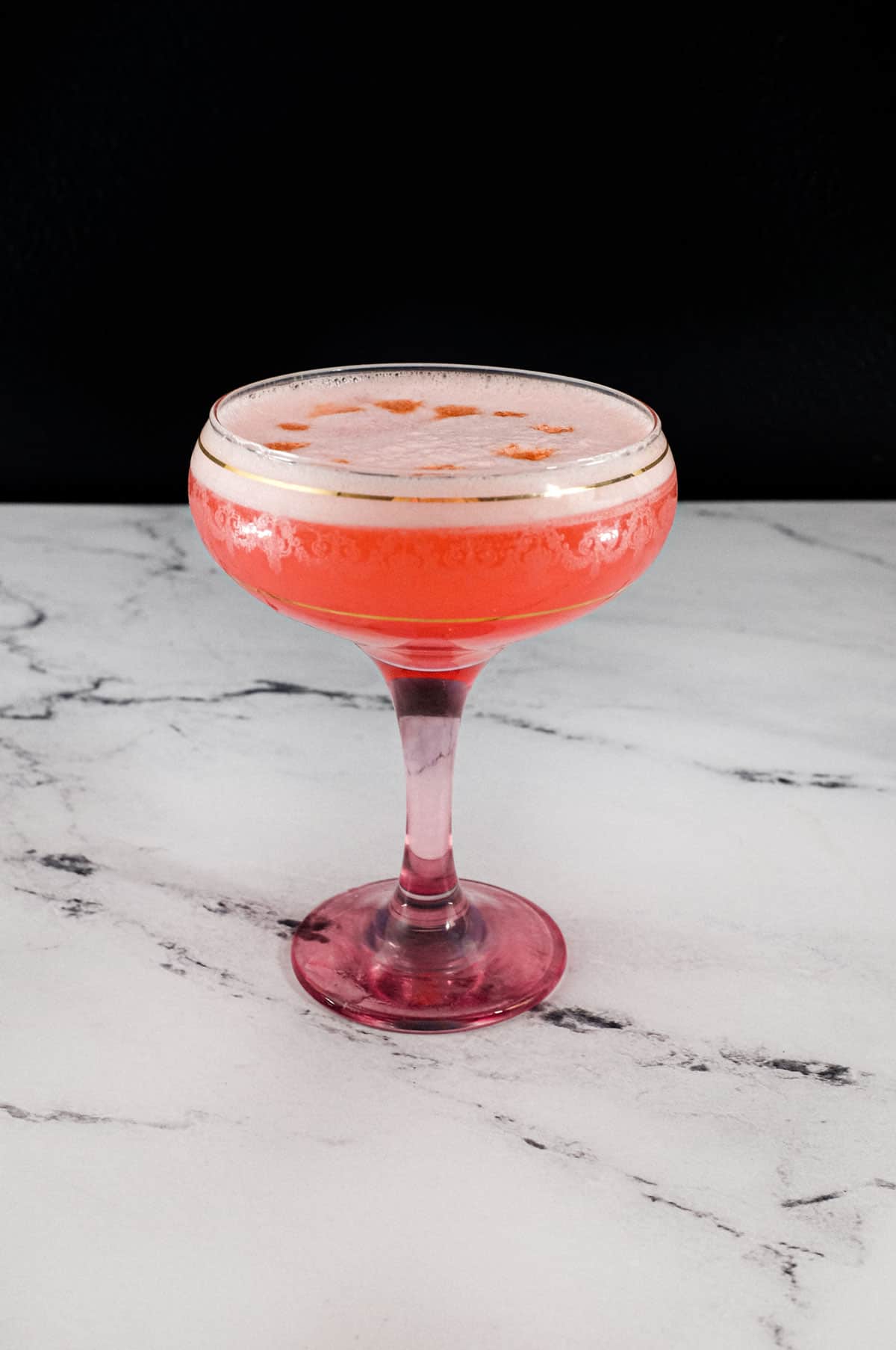 A pink Fizz cocktail with Campari and gin sits in a vintage Champagne glass