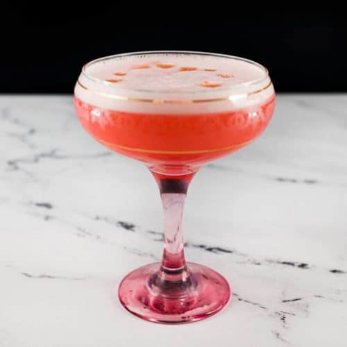 A pink Fizz cocktail with Campari and gin sits in a vintage Champagne glass