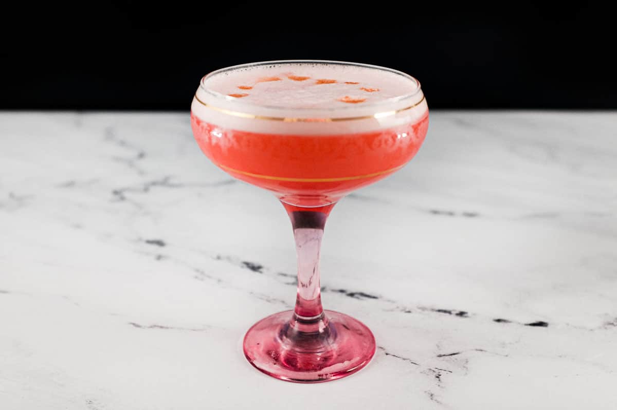 A pink Fizz cocktail with Campari and gin sits in a vintage Champagne glass