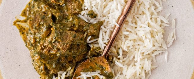 A plate of Saag Gosht Curry (Lamb & Spicanch is served with rice on an antique green silk carpet