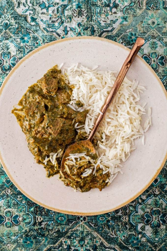 A plate of Saag Gosht Curry (Lamb & Spicanch is served with rice on an antique green silk carpet