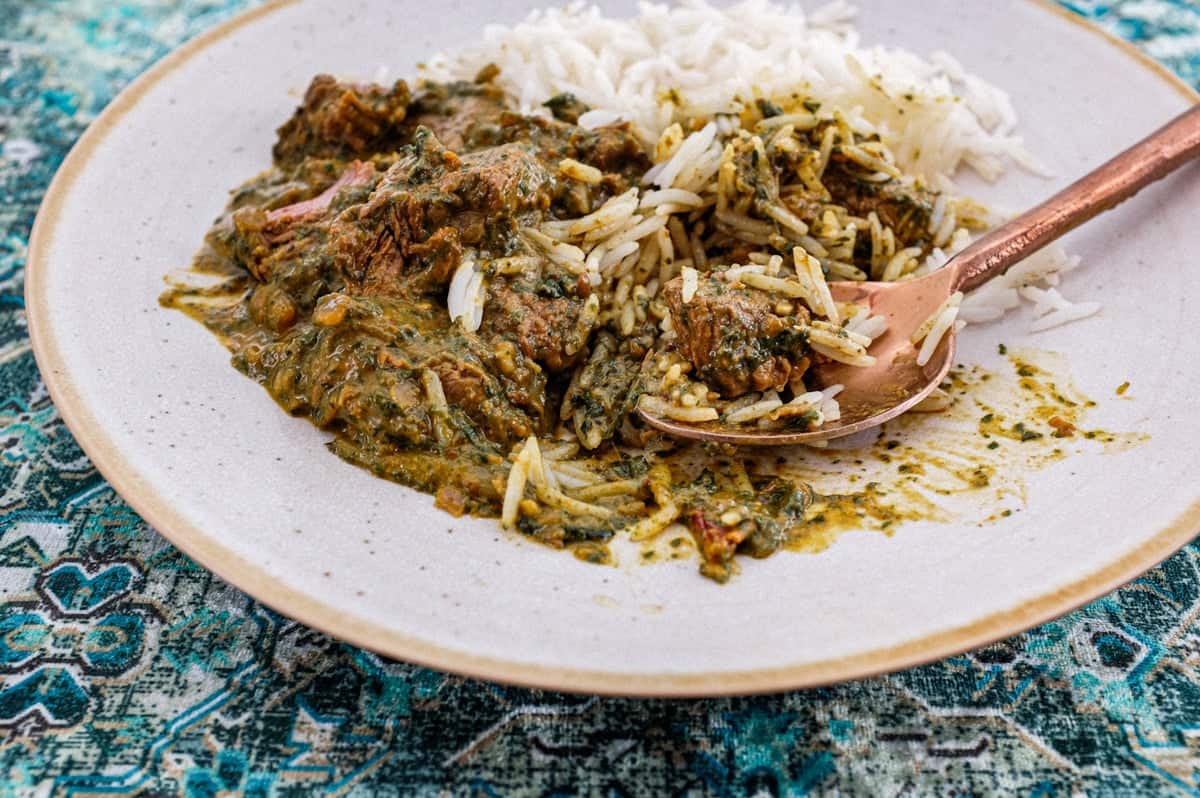 A plate of Saag Gosht Curry (Lamb & Spicanch is served with rice on an antique green silk carpet