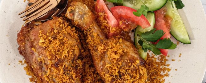 A platter of Ayam Serundeng fried chicken with crispy coconut with a side salad of cucumber and tomato