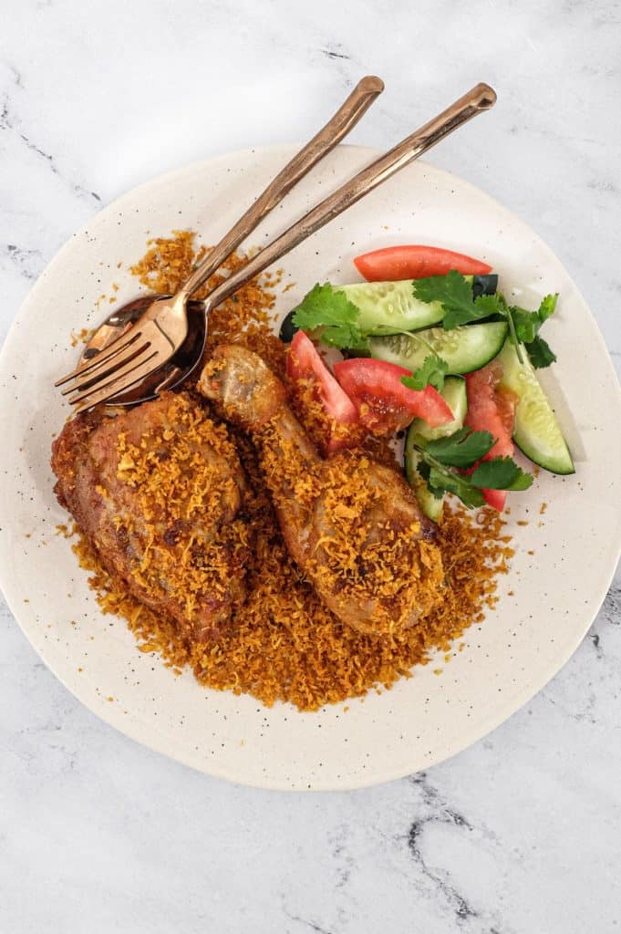 A platter of Ayam Serundeng fried chicken with crispy coconut with a side salad of cucumber and tomato