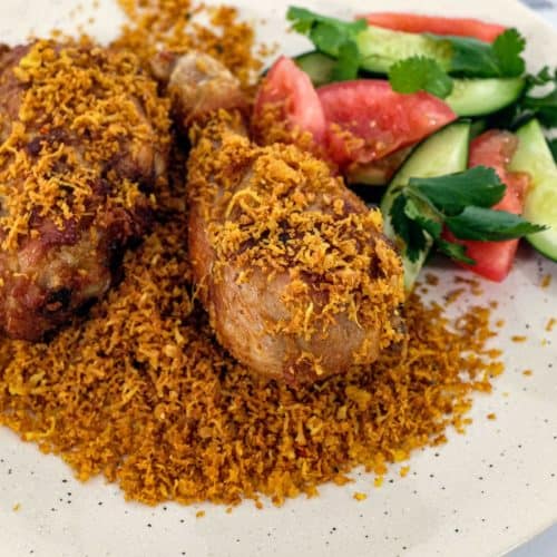 A platter of Ayam Serundeng fried chicken with crispy coconut with a side salad of cucumber and tomato