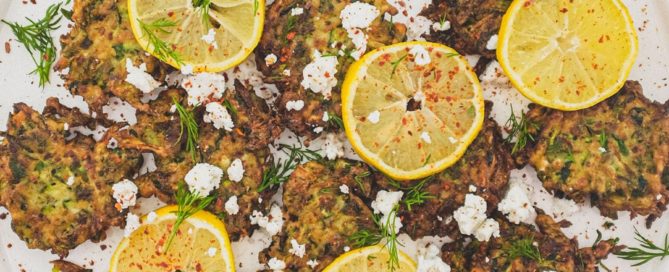 A platter of zucchini fritters with feta cheese and lemon slices