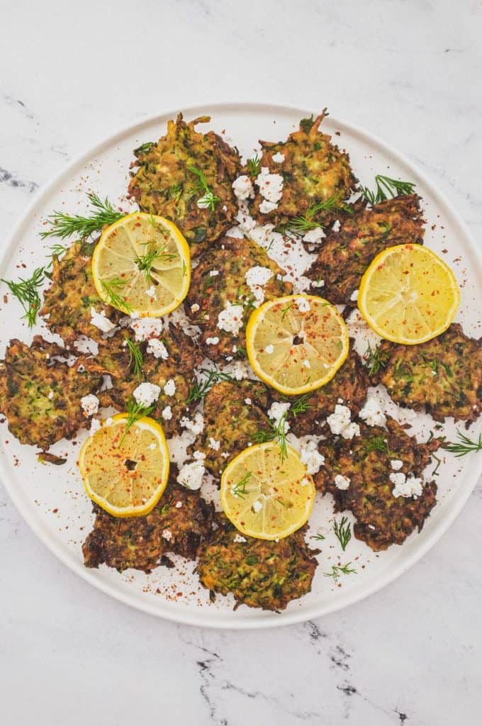 A platter of zucchini fritters with feta cheese and lemon slices