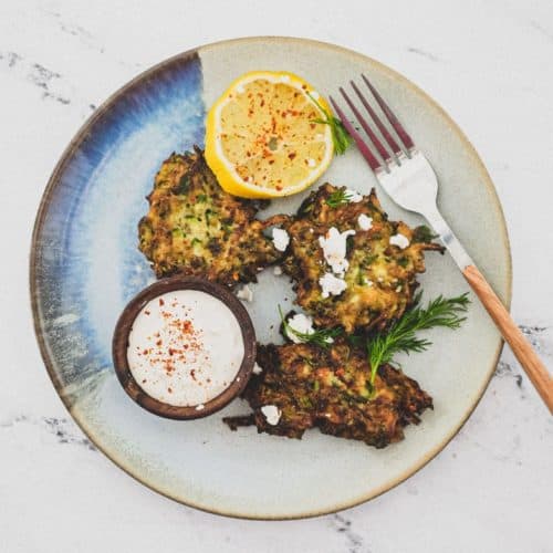 A platter of zucchini fritters with feta cheese and lemon slices