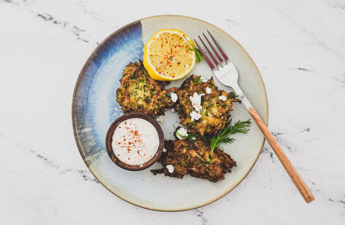 A platter of zucchini fritters with feta cheese and lemon slices