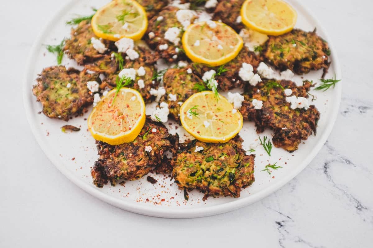 A platter of zucchini fritters with feta cheese and lemon slices