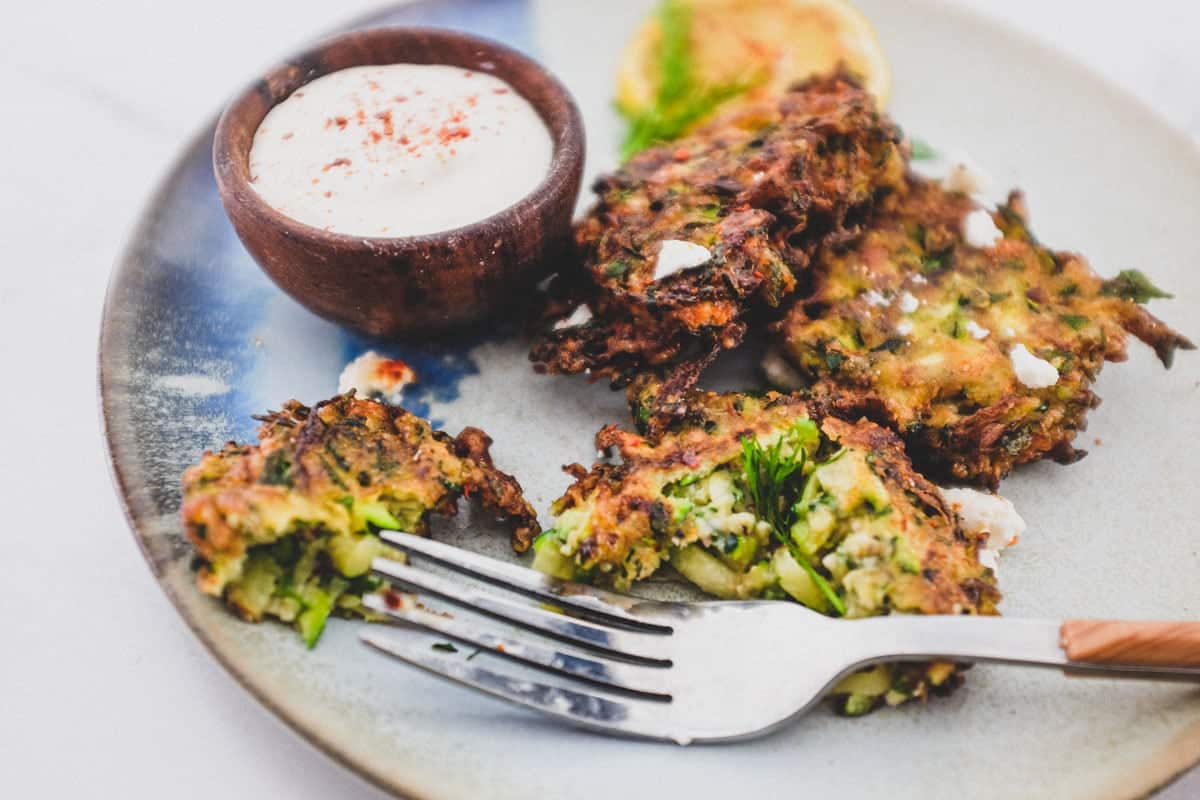 A platter of zucchini fritters with feta cheese and lemon slices