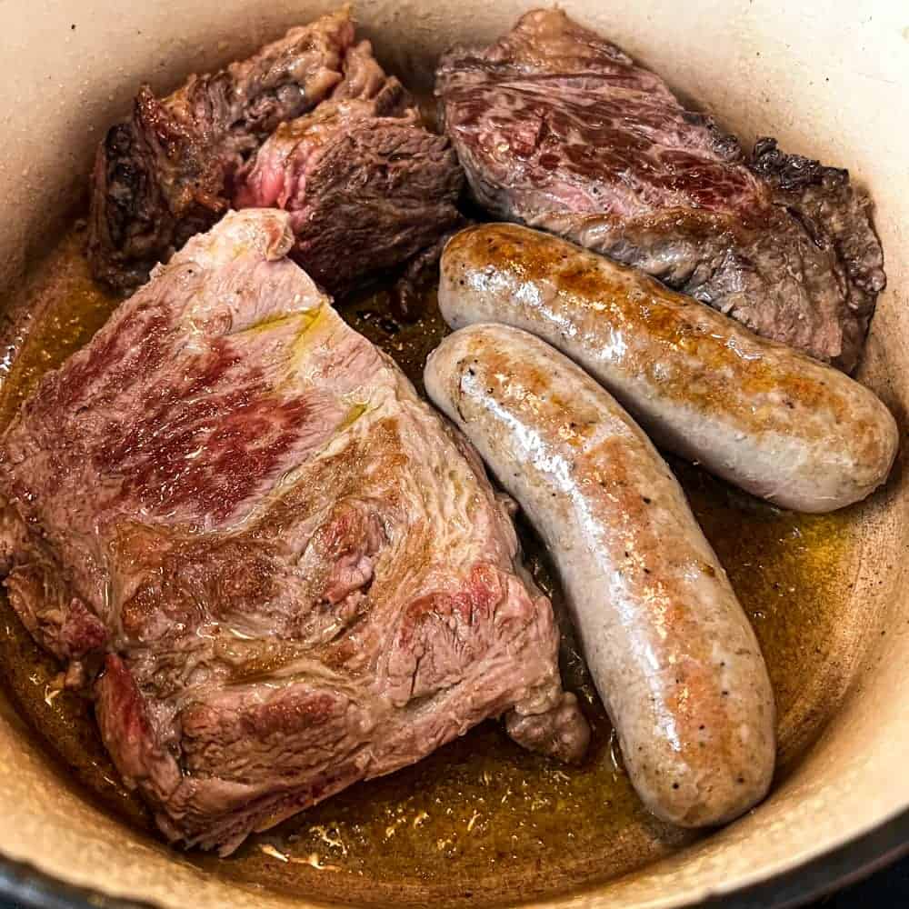 Sausage, pork and beef frying together in a large pan for the Neapolitan Ragù