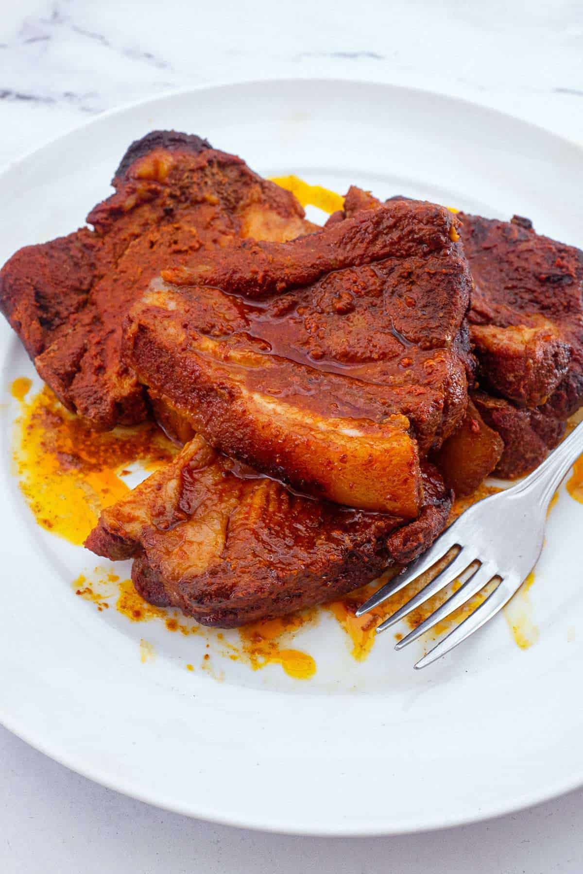 Slices of Pampanella Molisana, bright red slow-roasted pork in paprika on a plate with a fork