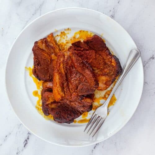 Slices of Pampanella Molisana, bright red slow-roasted pork in paprika on a plate with a fork