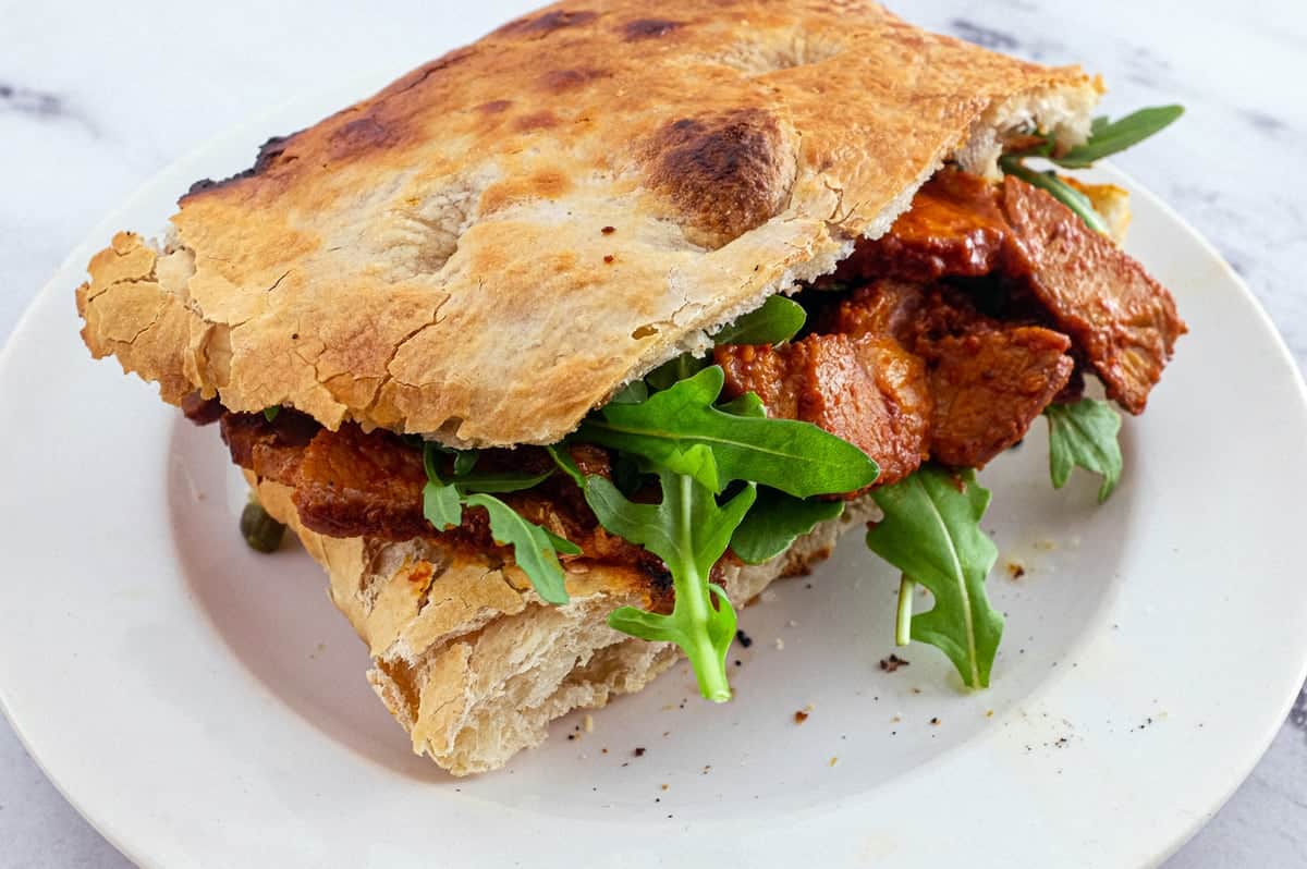 Slices of Pampanella Molisana, bright red slow-roasted pork in paprika in a sandwich of ciabatta bread with rocket leaves