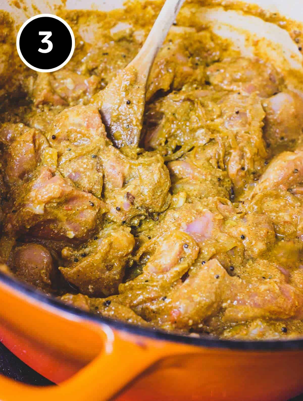 Chicken and spices cook in a large pan for Achari Chicken Curry