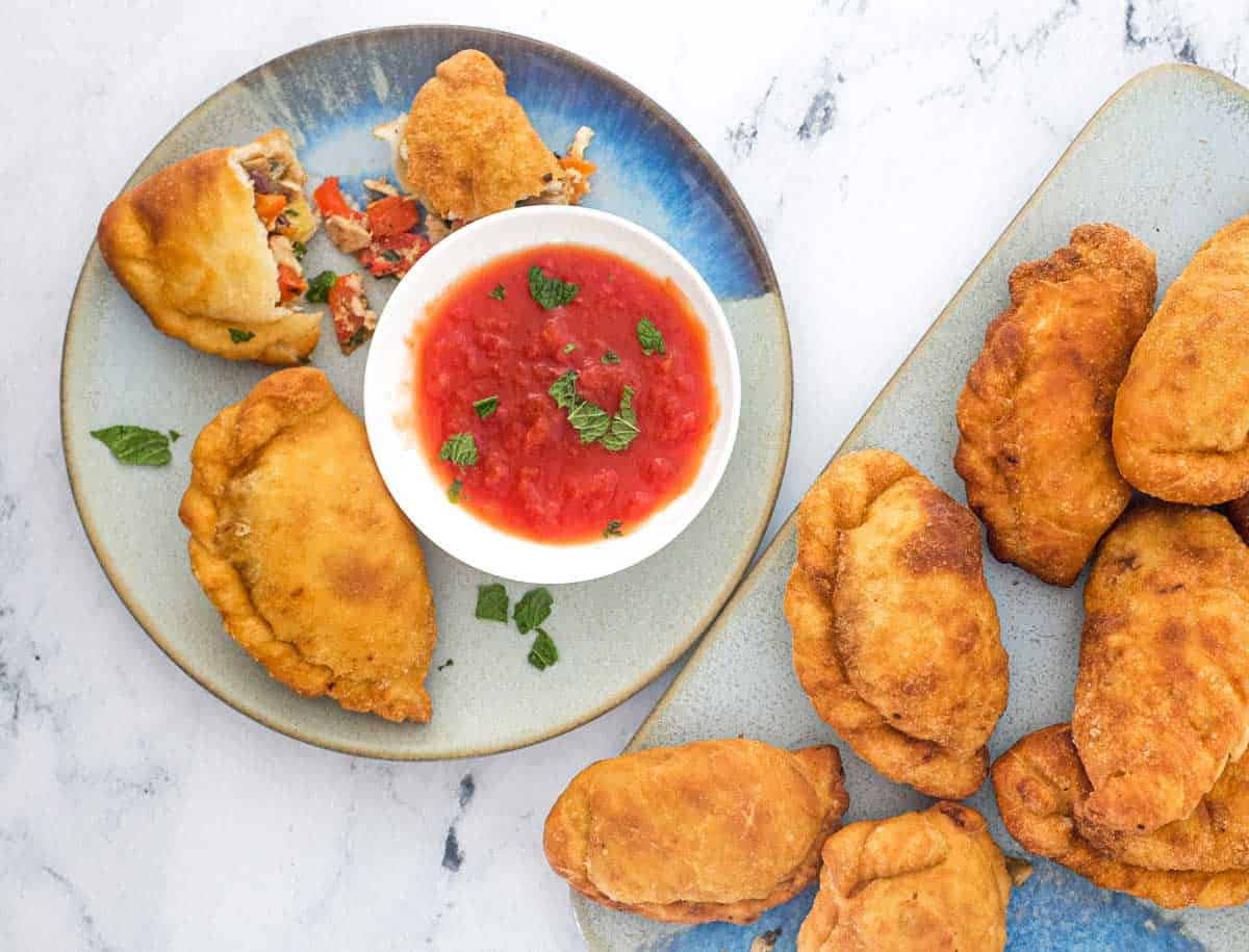Panzerotti sits on a plate with the filling on show of olives, tuna, egg and red pepper alongside a small dish of tomato sauce