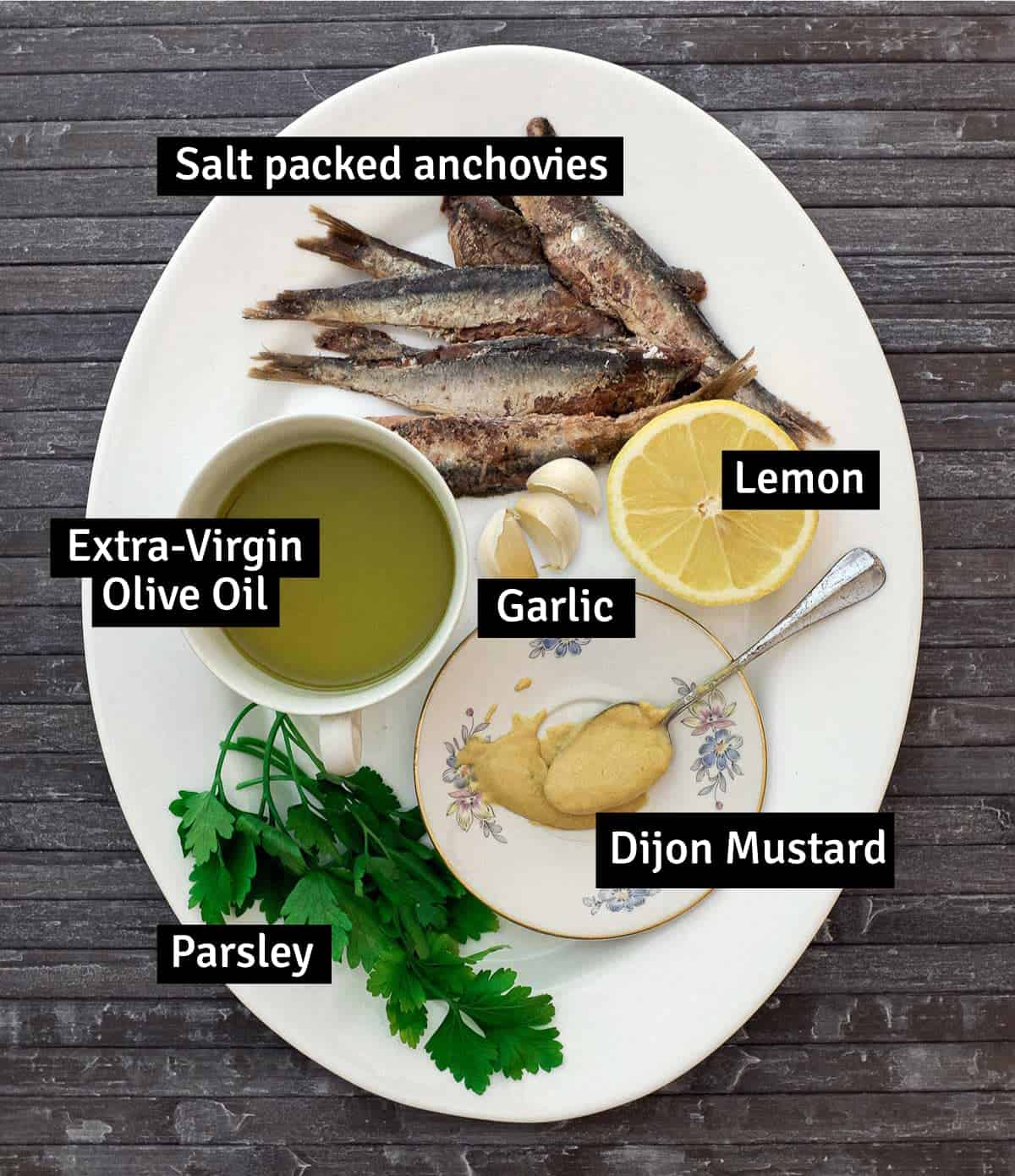 The Ingredients for Anchovy sauce on a large platter: Anchovies, Lemon, Dijon mustard, garlic, extra-virgin olive oil and parsley.