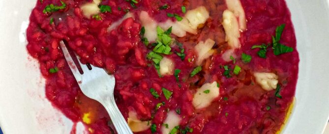 A bowl of beetroot risotto scattered with Taleggio cheese and fresh parsley on an Italian tiled background.