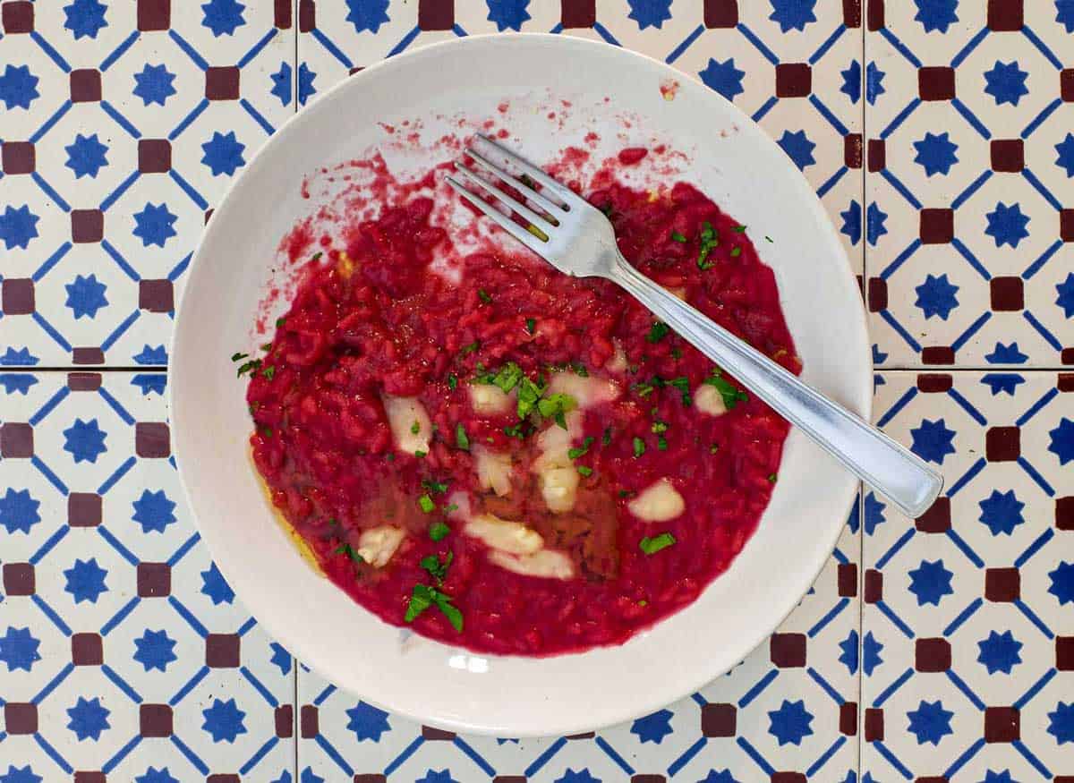 A bowl of beetroot risotto scattered with Taleggio cheese and fresh parsley on an Italian tiled background.