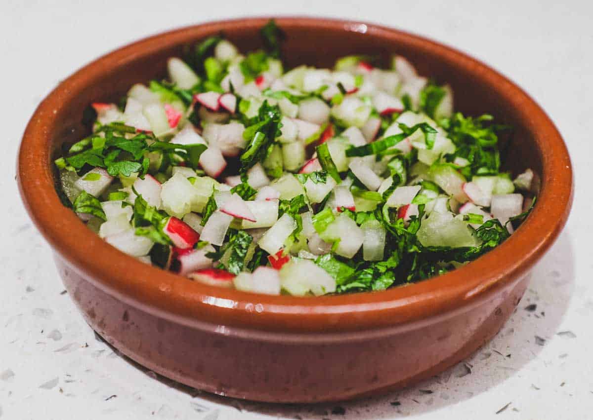 Garnishes for a fish curry in a terracotta bowl - radishes, cilantro and celery.