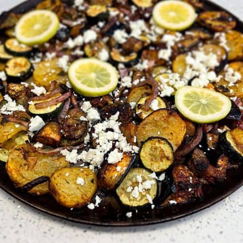 A platter of Greek Roasted Vegetables called Briam scattered with feta cheese and lemon slices