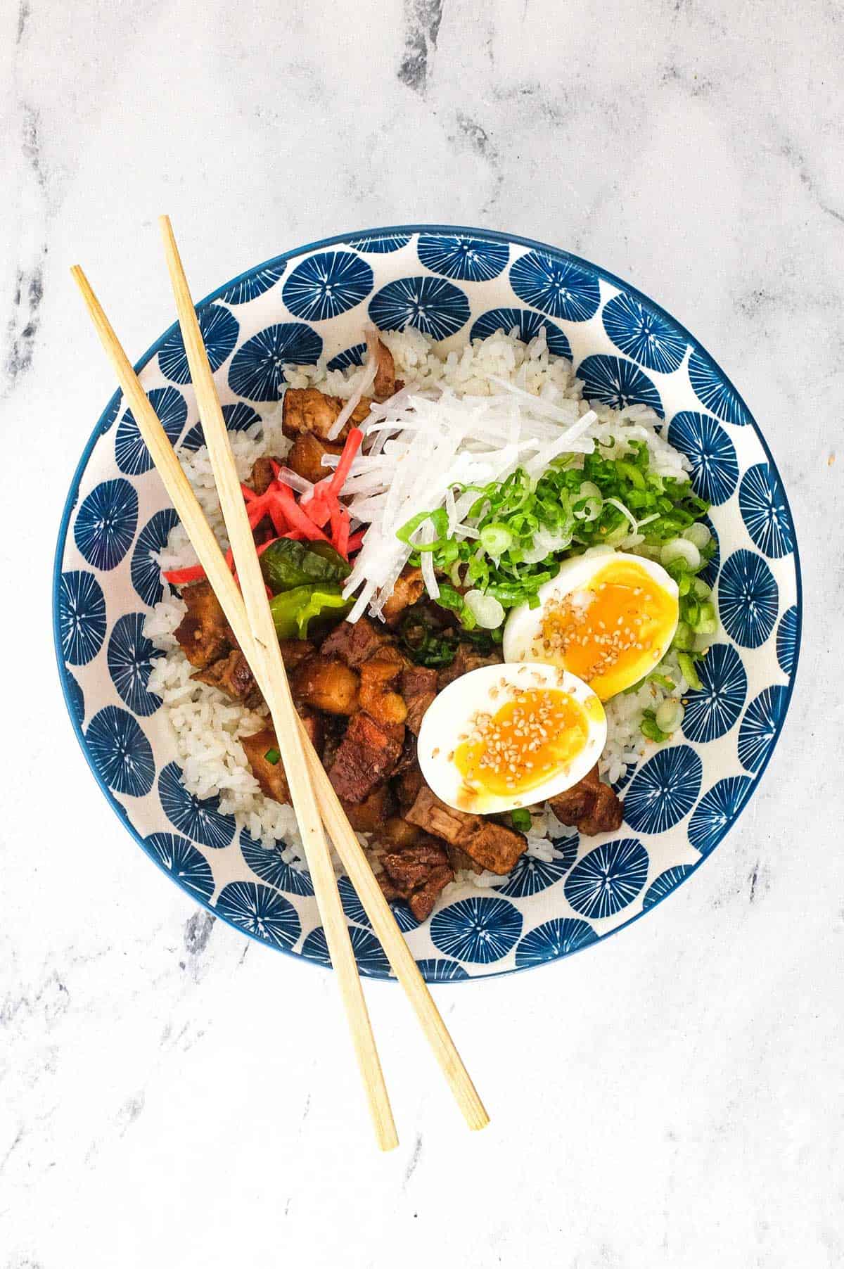 A Japanese pork rice bowl with chopsticks pork, spring onion, egg, radish and pickles.