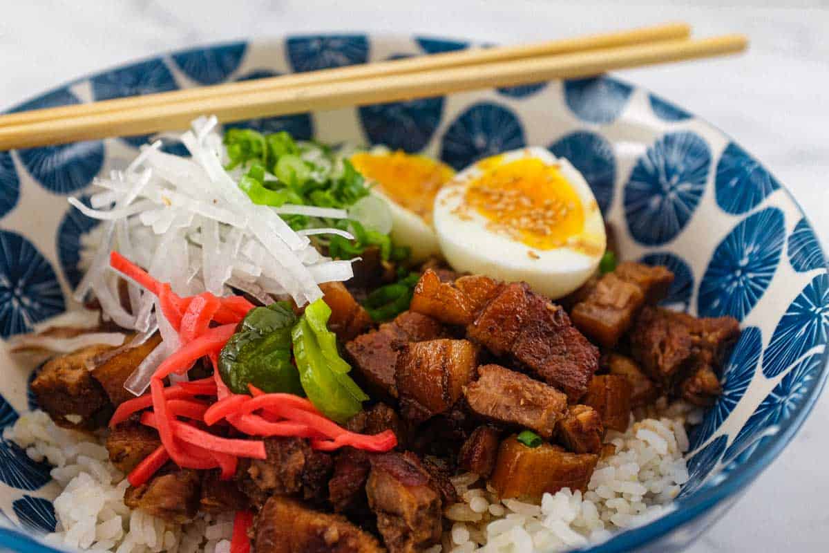 A Japanese pork rice bowl with chopsticks pork, spring onion, egg, radish and pickles.