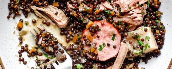A bowl of lentils with flaked pork and smoked sausages, scattered with fresh parsley | Salt Pork with Puy Lentils (Petit Sale aux Lentilles)