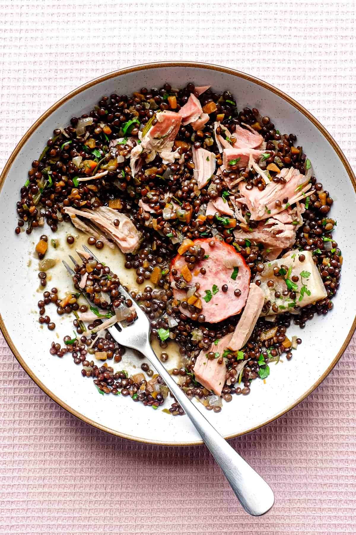 A bowl of lentils with flaked pork and smoked sausages, scattered with fresh parsley | Salt Pork with Puy Lentils (Petit Sale aux Lentilles)