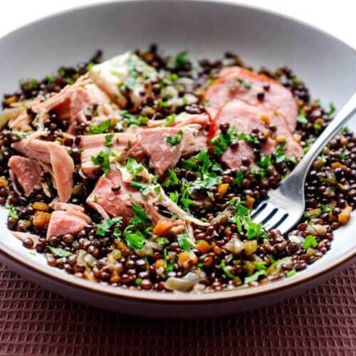 A bowl of lentils with flaked pork and smoked sausages, scattered with fresh parsley | Salt Pork with Puy Lentils (Petit Sale aux Lentilles)