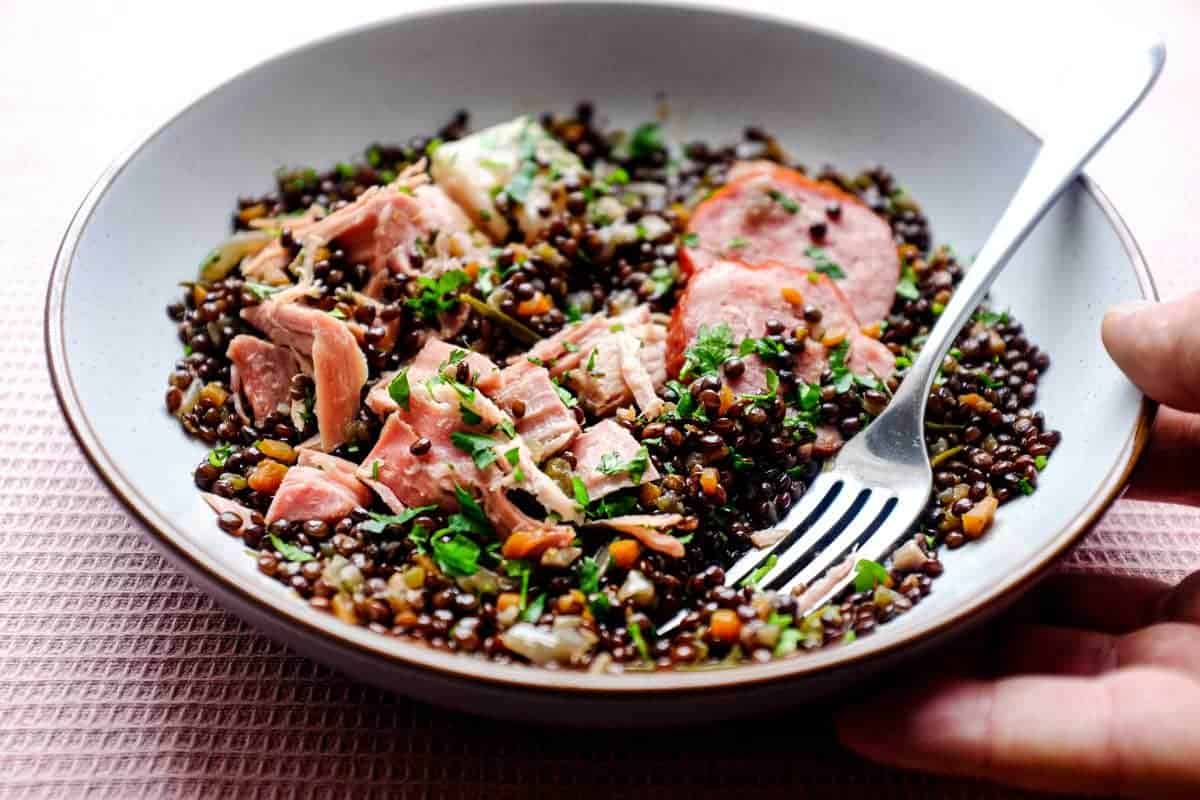 A bowl of lentils with flaked pork and smoked sausages, scattered with fresh parsley | Salt Pork with Puy Lentils (Petit Sale aux Lentilles)