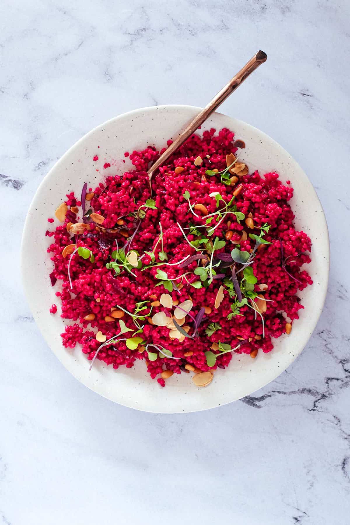 Israeli Couscous with BeetrootA on a plate, scattered with micro greens and nuts.