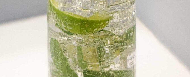 A glass of sparkling Hugo Spritz cocktail with ice, mint and limes
