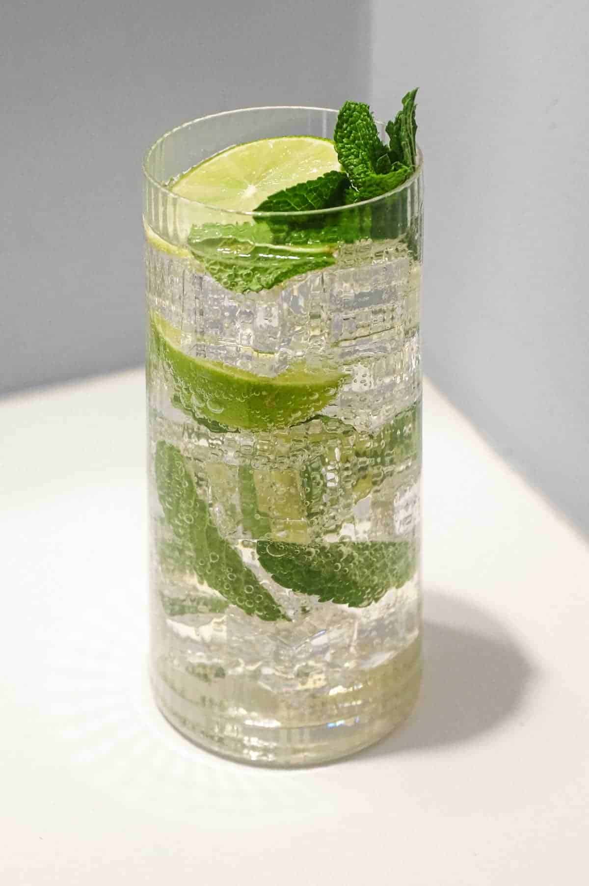 A glass of sparkling Hugo Spritz cocktail with ice, mint and limes