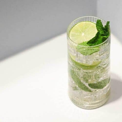A glass of sparkling Hugo Spritz cocktail with ice, mint and limes