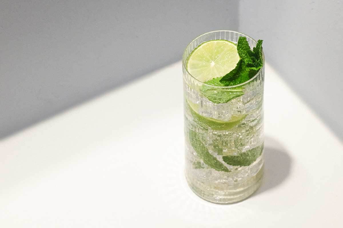 A glass of sparkling Hugo Spritz cocktail with ice, mint and limes