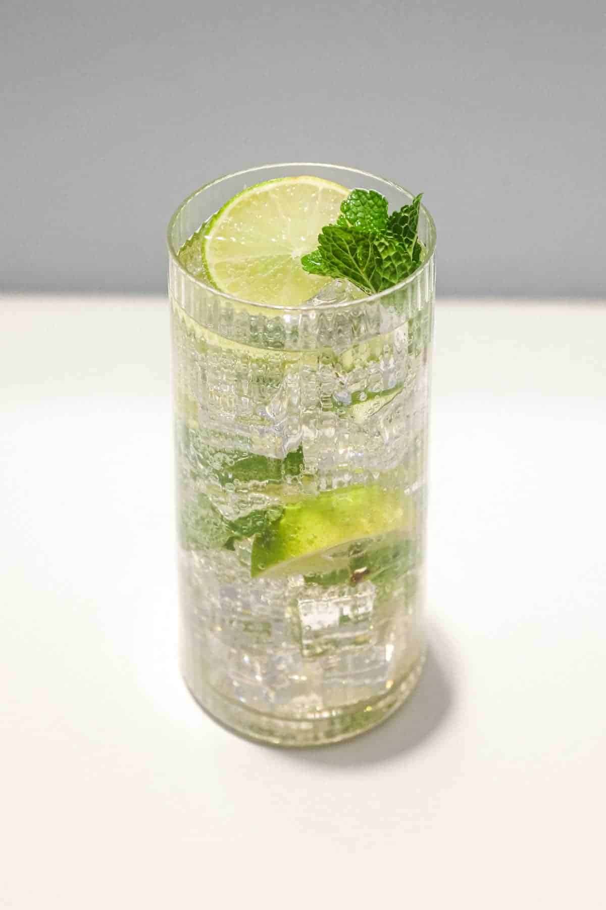 A glass of sparkling Hugo Spritz cocktail with ice, mint and limes