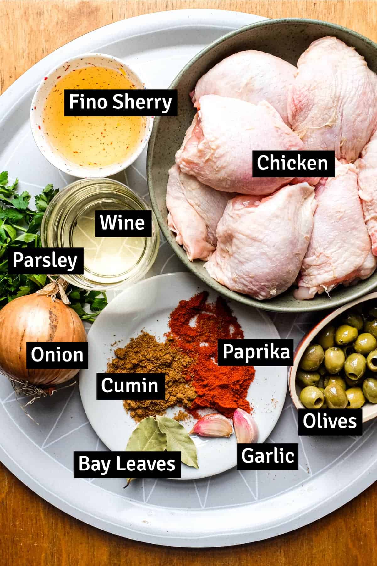 The ingredients for Spanish Chicken including chicken thighs, wine, sherry, onion, garlic, parsley, olives, paprika, cumin and bay leaf.