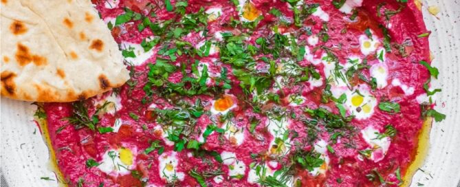 A bowl of beetroot dip scattered with herbs and yoghurt, served with flatbreads