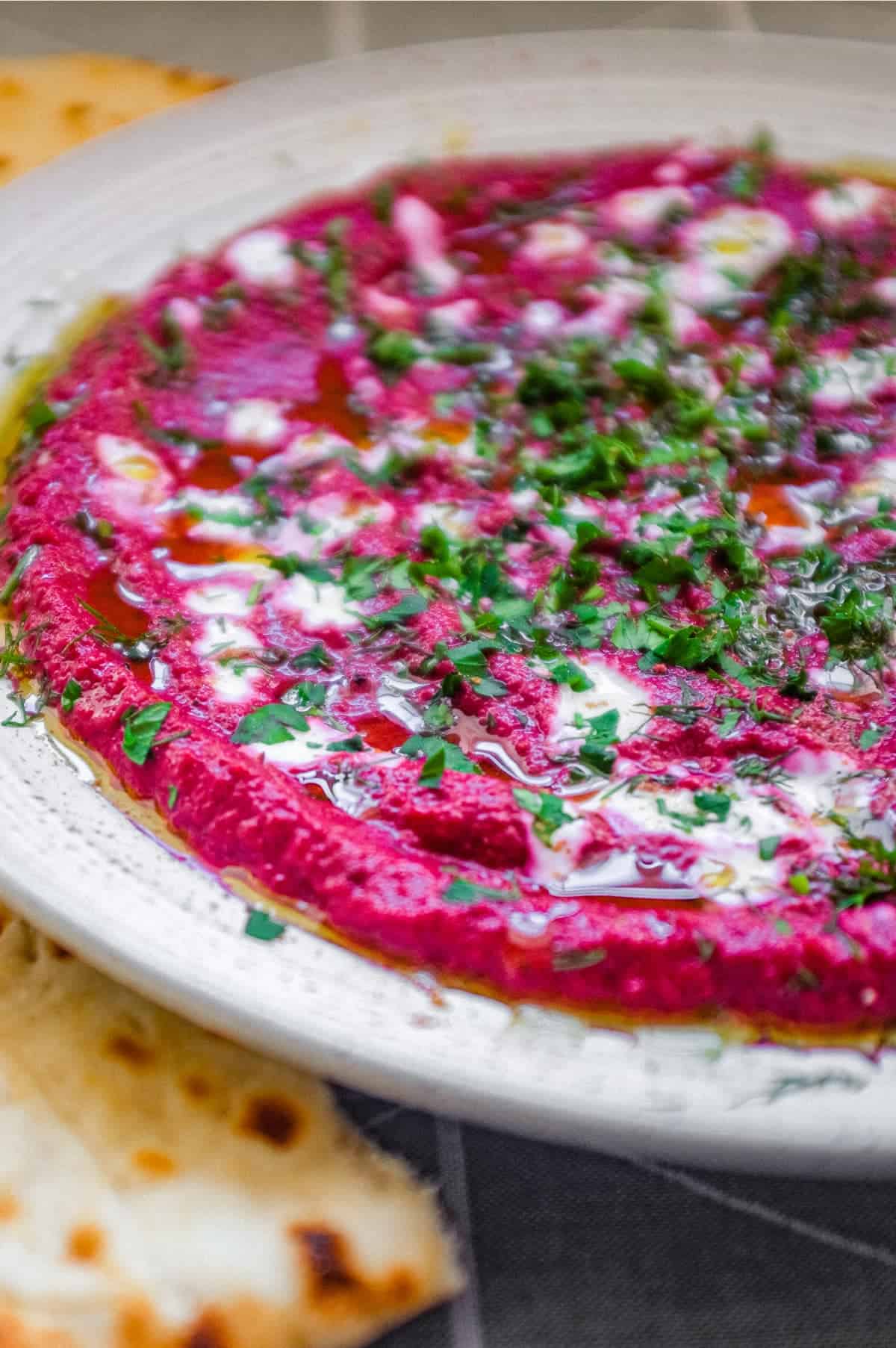 A bowl of beetroot dip scattered with herbs and yoghurt, served with flatbreads