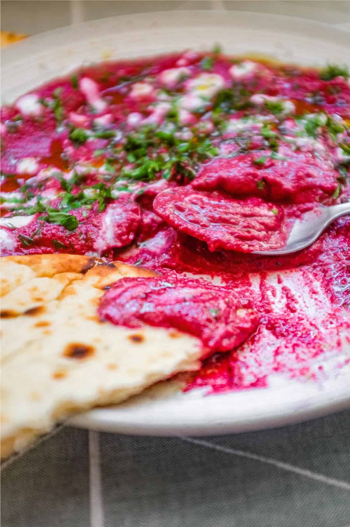 A bowl of beetroot dip scattered with herbs and yoghurt, served with flatbreads