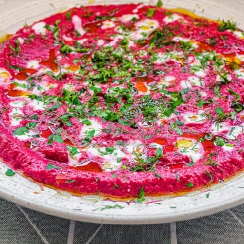 A bowl of beetroot dip scattered with herbs and yoghurt, served with flatbreads