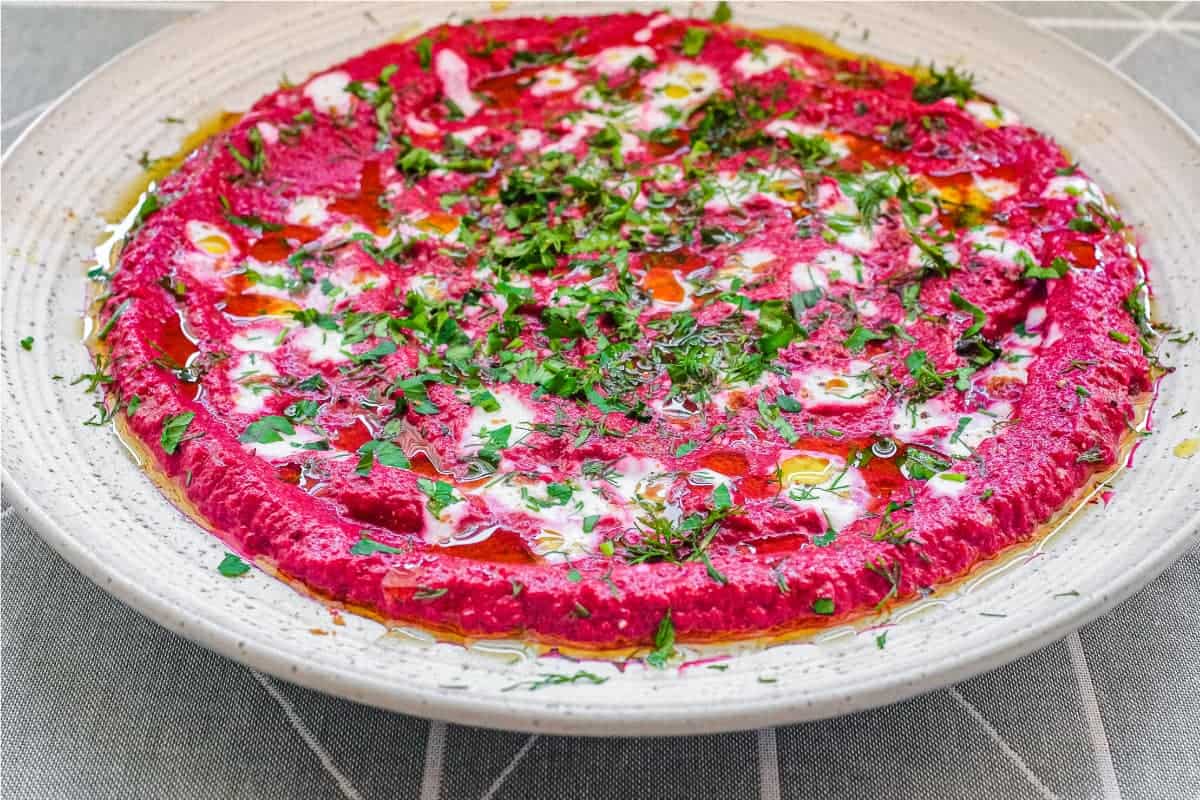 A bowl of beetroot dip scattered with herbs and yoghurt, served with flatbreads