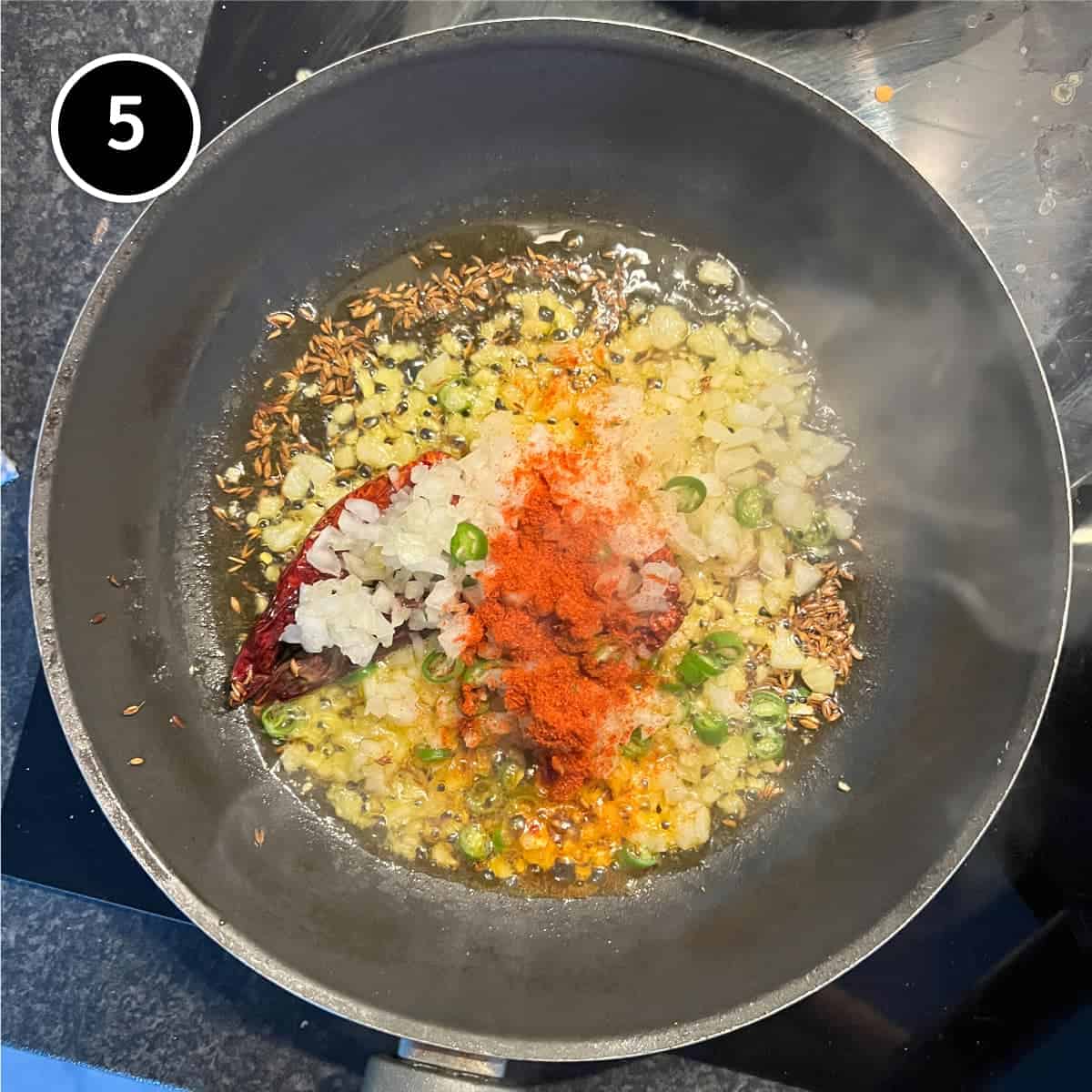 Making a tadka - frying onion, cumin seeds, chilli and spice in hot mustard oil in a small frying pan.