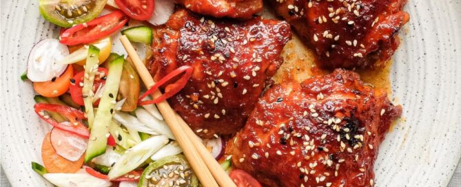 A plate of Korean Gochujang Chicken and chopsticks with salad on the side.