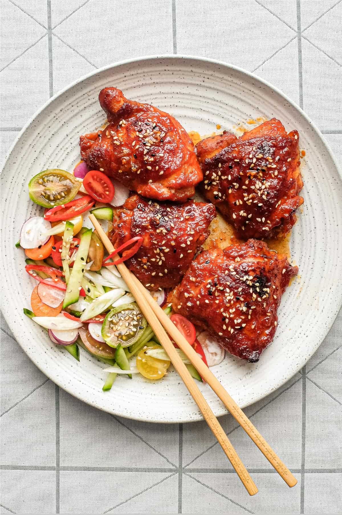A plate of Korean Gochujang Chicken and chopsticks with salad on the side.