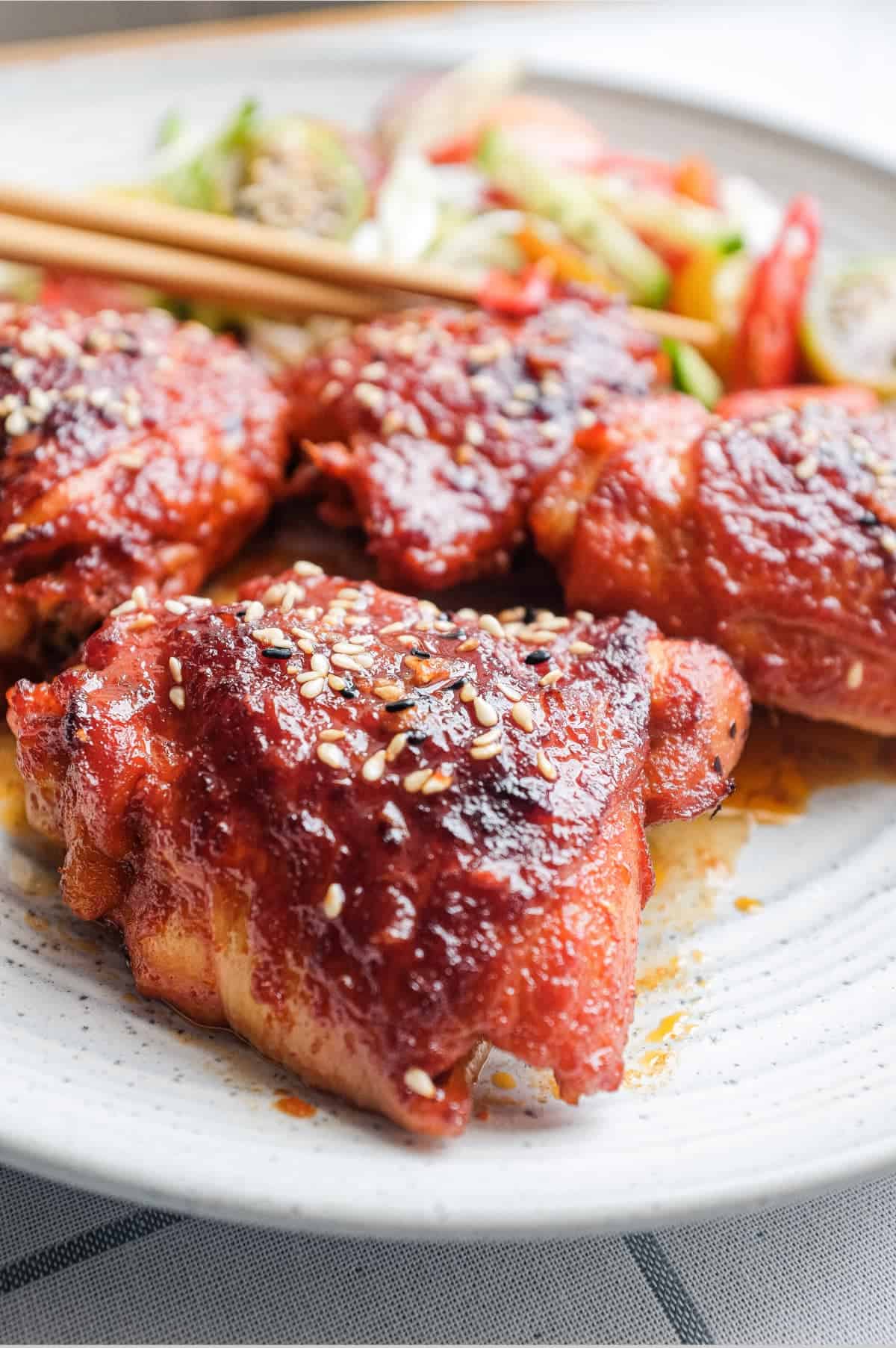 A plate of Korean Gochujang Chicken and chopsticks with salad on the side.